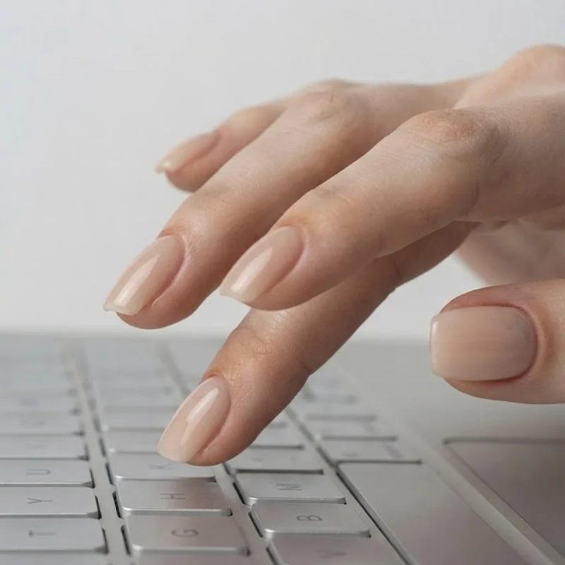 Best nail shape for typing shown on hands mid-keystroke in a short almond gel manicure at a home desk setup